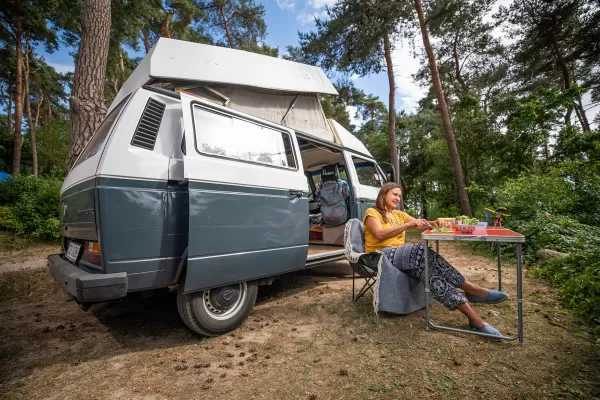 Eine Frau isst vor ihrem Camper im Wald. 