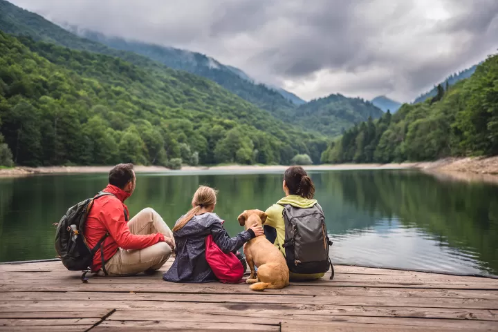 Familie mit Hund sitzt an einem See im Wald in den Bergen.