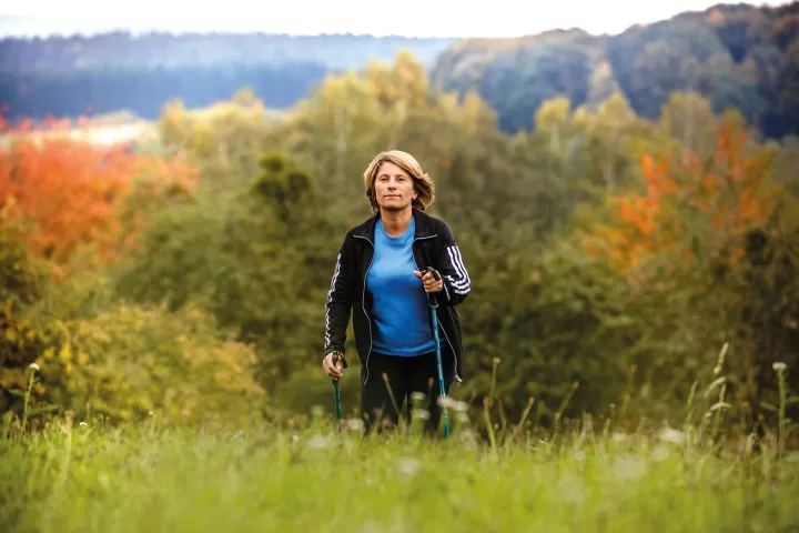 Frau überquert beim Nordic Walking eine Wiese.